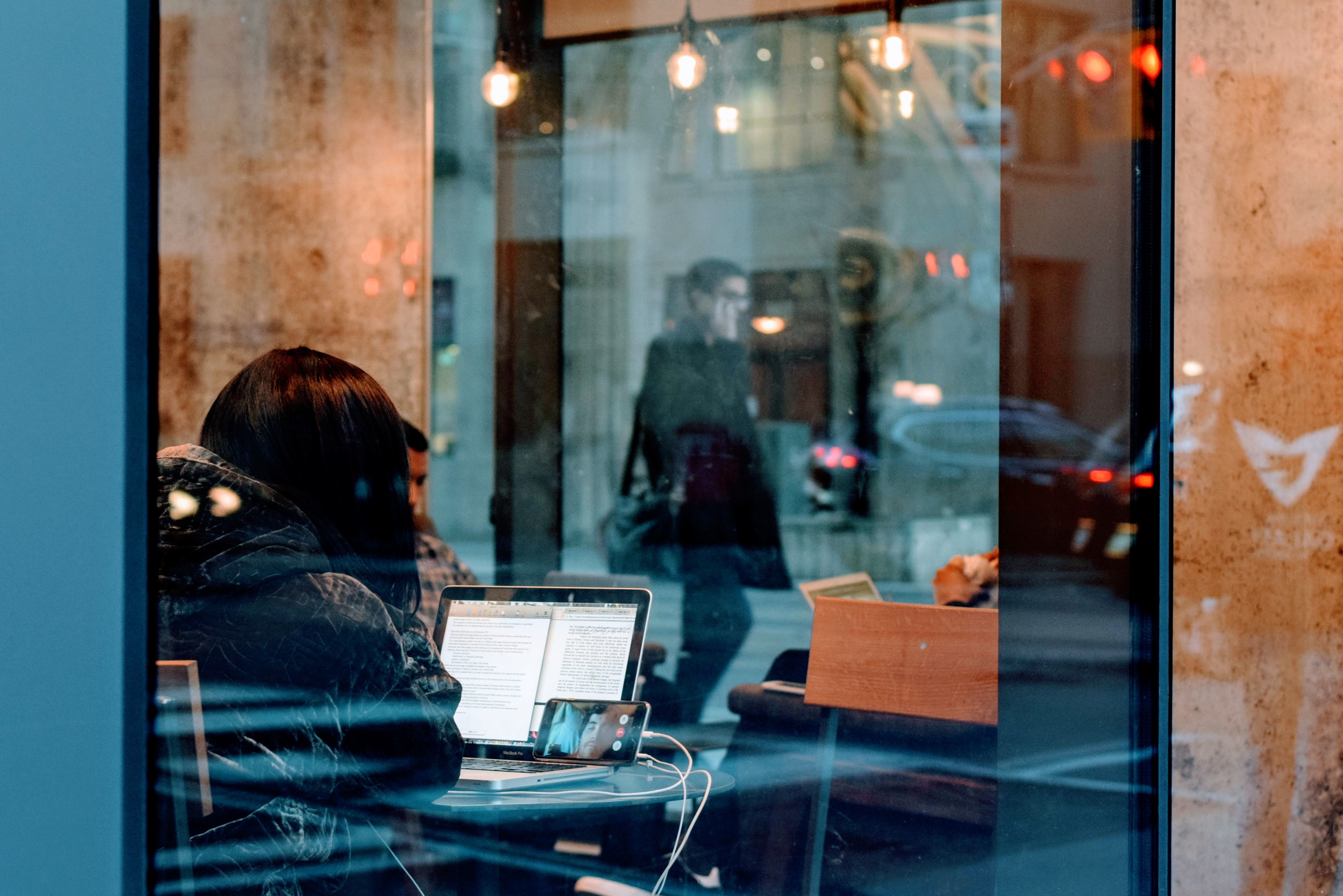 Staring into a glass window from a street in Toronto at a female looking at her phone and computer